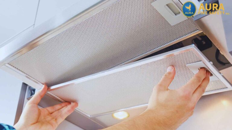 Showing the process of kitchen maintenance, a pair of hands grasp the edge of a grease filter, pulling it down from a professional-grade kitchen exhaust hood.