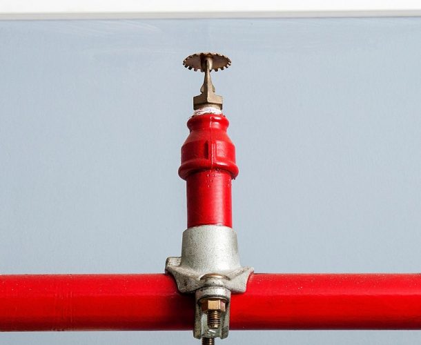 Close-up of a red fire sprinkler head on a matching pipe against a blue wall, exemplifying the critical components inspected during a fire sprinkler system inspection for safety assurance.