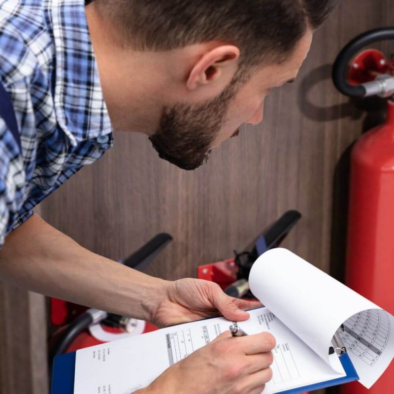 A meticulous technician performing a quarterly fire sprinkler inspection, carefully reviewing the checklist to ensure compliance and safety in a workplace environment.